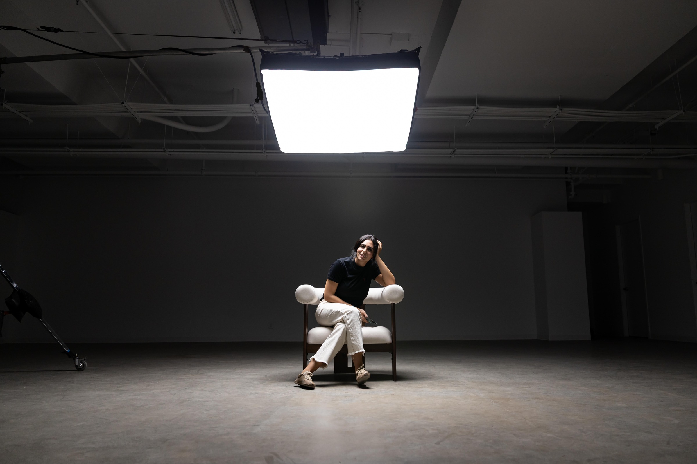 Mandana seated alone under a single studio light